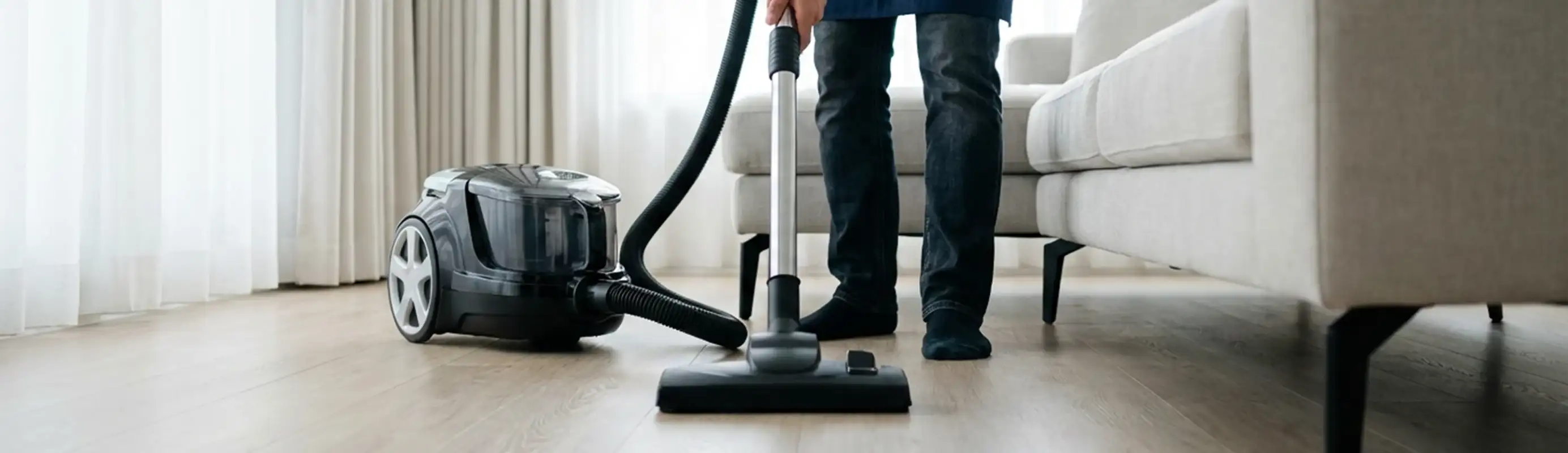 Professional house cleaner vacuuming a living room floor with a canister vacuum cleaner, Honolulu, HI.