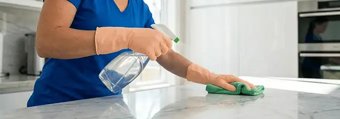 Maid service worker spraying and wiping a kitchen countertop with a microfiber cloth for sanitizing, Honolulu, HI.