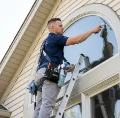 Professional window cleaner on a ladder using a squeegee to clean an exterior arched window, Honolulu, HI.