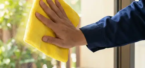 House cleaner wiping a glass window with a yellow microfiber cloth for streak-free cleaning, Honolulu, HI.